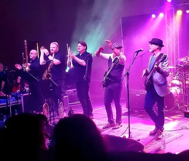 An image of five of the members of Midlife Crisis playing on a stage bathed in purple light.